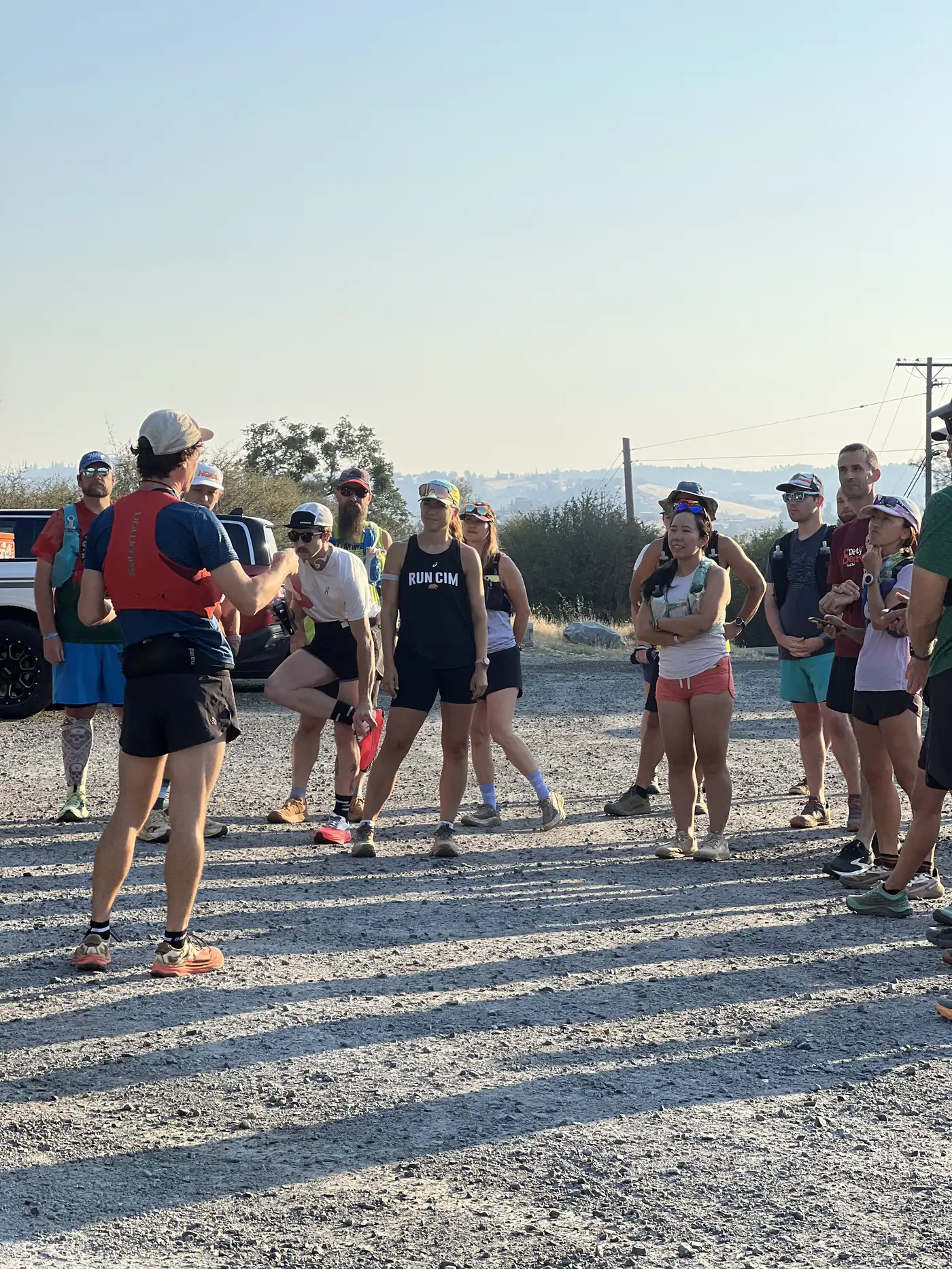 A group of runners listening to a pre-run briefing at a trailhead